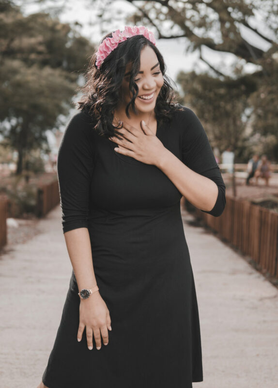 A joyful woman in a black dress with a pink floral headband, symbolizing the uplifting spirit of e3's Happy Heart Blend.