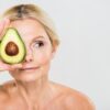 After a shower, a beautiful woman holds an avocado half up to her face denoting ways to combat chronic stress and skin problems